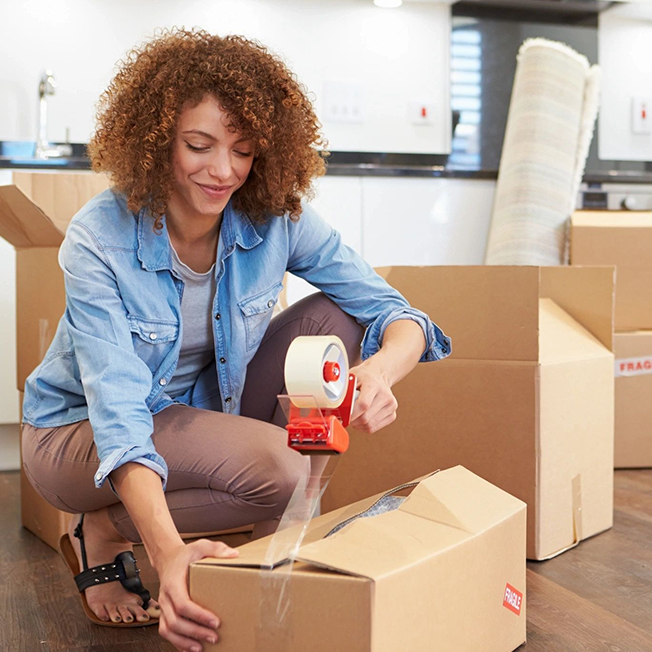 Woman Kneeling Down Sealing Boxes Ready For House Move